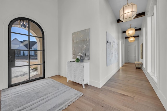 entryway with beamed ceiling, a towering ceiling, a healthy amount of sunlight, and light hardwood / wood-style flooring