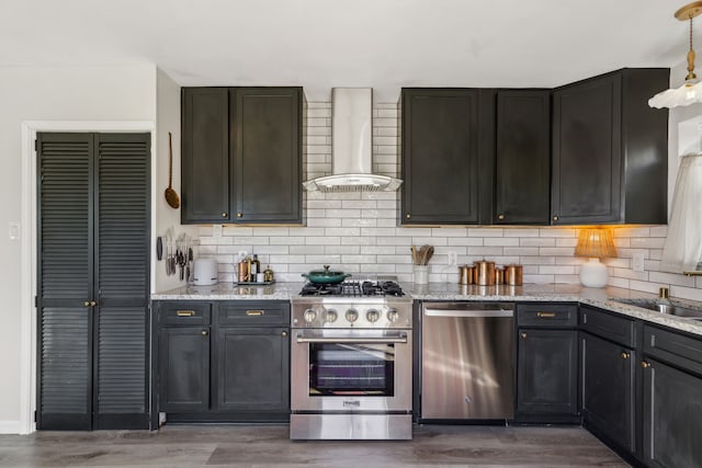 kitchen featuring stainless steel appliances, wood finished floors, light stone countertops, wall chimney exhaust hood, and tasteful backsplash