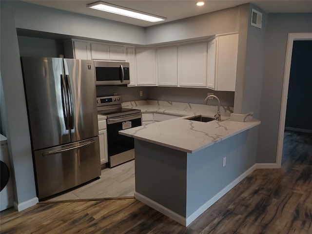 kitchen featuring sink, light stone counters, white cabinetry, wood-type flooring, and appliances with stainless steel finishes