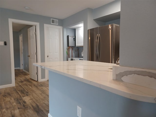 kitchen featuring dark wood-type flooring, light stone counters, stainless steel fridge, water heater, and white cabinets