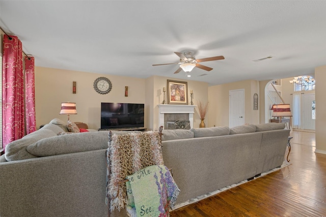 living room with hardwood / wood-style flooring, a tiled fireplace, and ceiling fan with notable chandelier