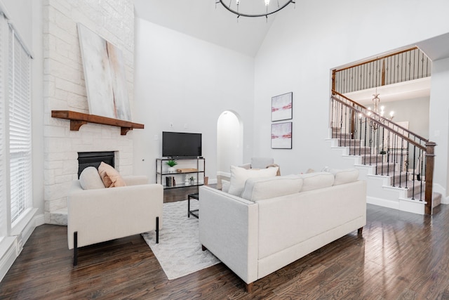 living room with high vaulted ceiling, dark wood-type flooring, a stone fireplace, and an inviting chandelier