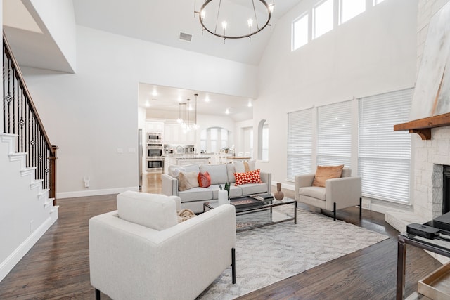 living room with a notable chandelier, a towering ceiling, a fireplace, and dark wood-type flooring