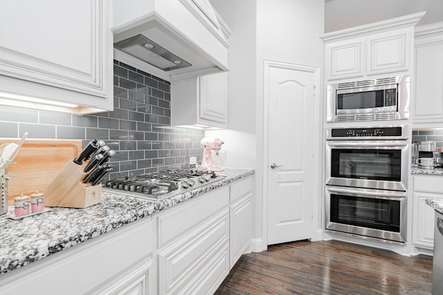 kitchen with light stone countertops, white cabinetry, appliances with stainless steel finishes, and custom range hood