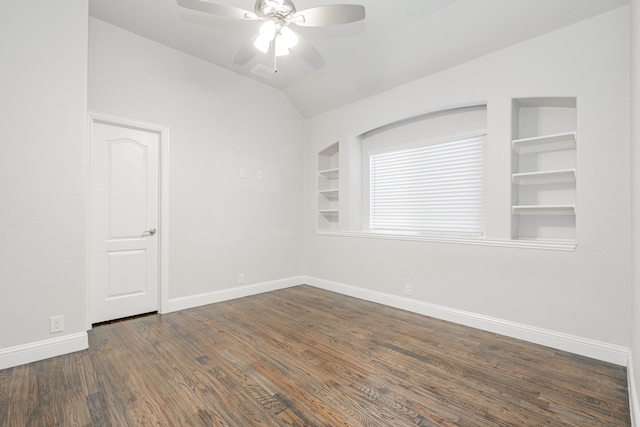 spare room with vaulted ceiling, dark hardwood / wood-style floors, ceiling fan, and built in shelves