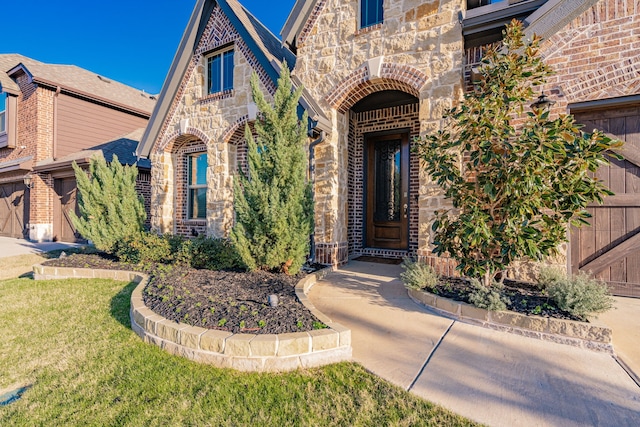 1108 Canterbury Ln, Forney, TX 75126 - view of exterior entry featuring stone siding, brick siding, a lawn, and a garage