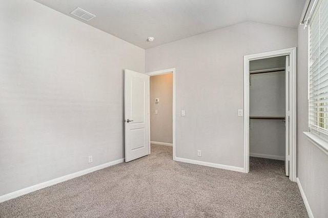 unfurnished bedroom featuring light carpet, a walk in closet, a closet, and vaulted ceiling