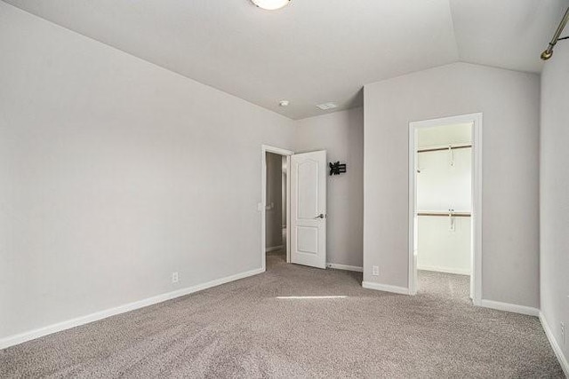 unfurnished bedroom featuring carpet flooring, a spacious closet, vaulted ceiling, and a closet