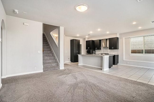 kitchen with light carpet, wall chimney range hood, tasteful backsplash, and a center island with sink