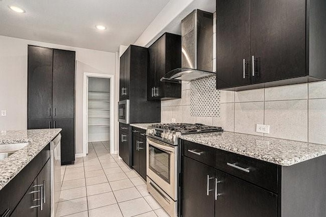 kitchen featuring wall chimney range hood, light tile patterned floors, backsplash, stainless steel appliances, and light stone counters