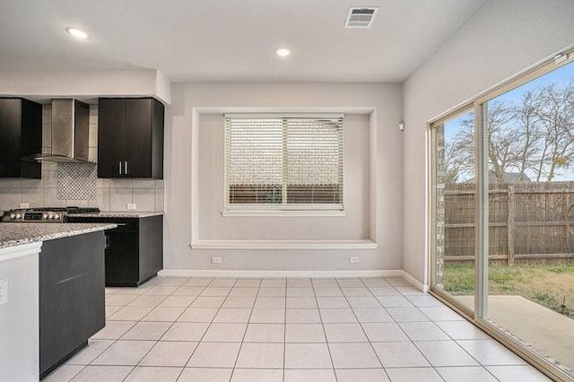 kitchen with light stone counters, backsplash, light tile patterned floors, and wall chimney exhaust hood