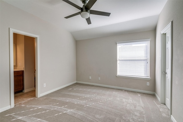 unfurnished bedroom featuring lofted ceiling, connected bathroom, light colored carpet, and ceiling fan