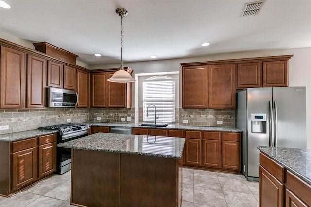 kitchen featuring sink, stainless steel appliances, a center island, and dark stone counters