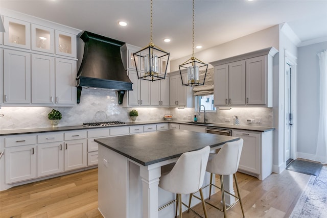 kitchen with white cabinetry, a kitchen island, decorative light fixtures, custom exhaust hood, and light wood-type flooring