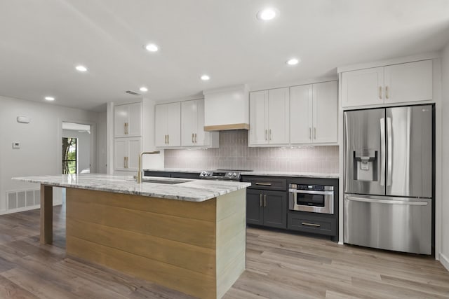 kitchen featuring sink, premium range hood, a kitchen island with sink, appliances with stainless steel finishes, and white cabinets