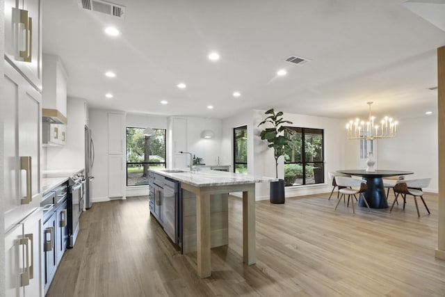 kitchen with sink, white cabinetry, hanging light fixtures, a center island with sink, and light stone countertops