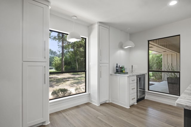 bar with wine cooler, pendant lighting, white cabinets, and light hardwood / wood-style floors