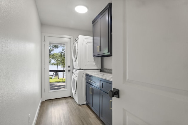 laundry room featuring light hardwood / wood-style floors, cabinets, and stacked washing maching and dryer