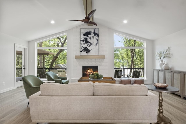 living room featuring a fireplace, light hardwood / wood-style flooring, ceiling fan, and vaulted ceiling