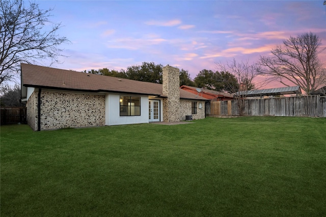 back house at dusk featuring a lawn