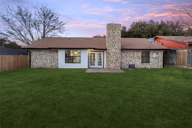 back house at dusk featuring a patio, a yard, and french doors