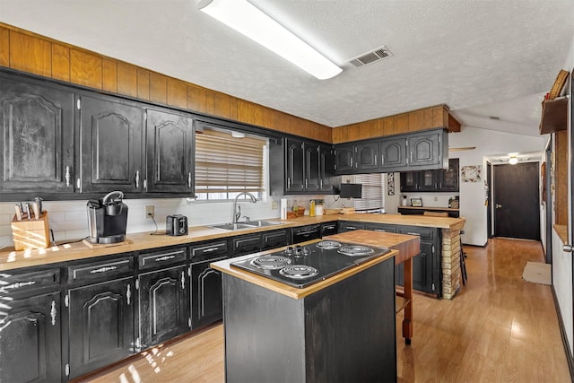 kitchen with a kitchen island, butcher block counters, sink, a textured ceiling, and light hardwood / wood-style flooring