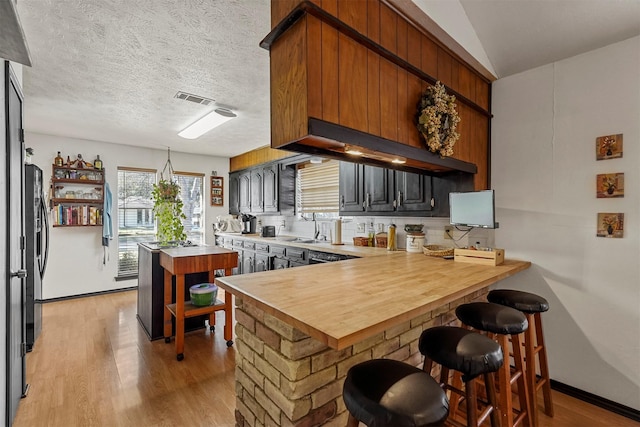 kitchen featuring backsplash, a kitchen breakfast bar, light hardwood / wood-style floors, kitchen peninsula, and a textured ceiling