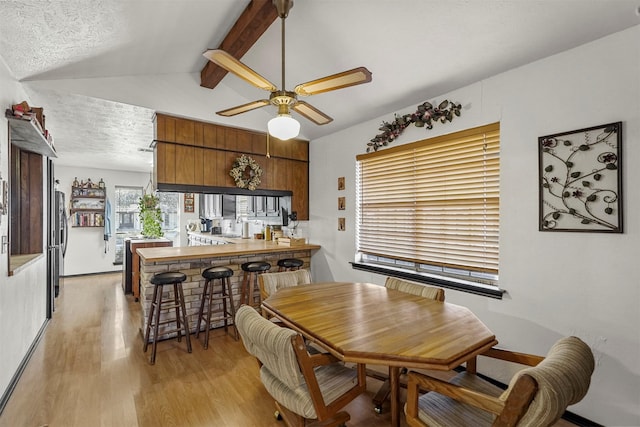 dining room featuring ceiling fan, light wood-type flooring, a textured ceiling, and vaulted ceiling with beams