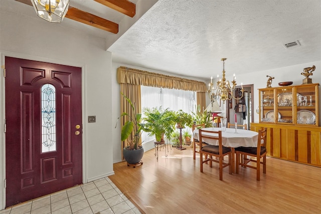 foyer with an inviting chandelier, beam ceiling, a textured ceiling, and light tile patterned floors