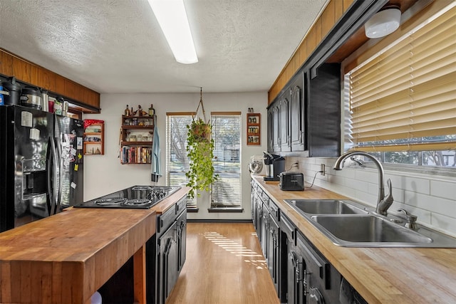 kitchen with sink, tasteful backsplash, black appliances, a textured ceiling, and light wood-type flooring