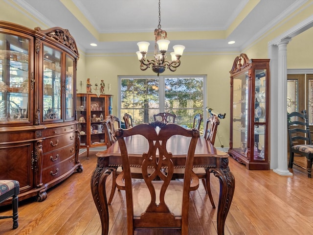 dining area with a tray ceiling, decorative columns, light hardwood / wood-style floors, and a chandelier