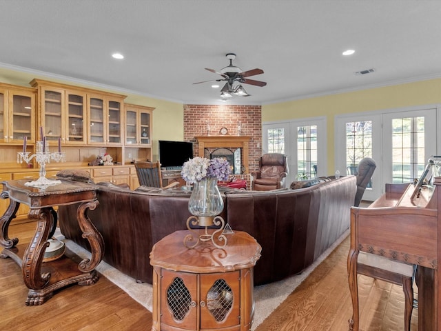 living room featuring crown molding, a brick fireplace, ceiling fan, and light hardwood / wood-style flooring