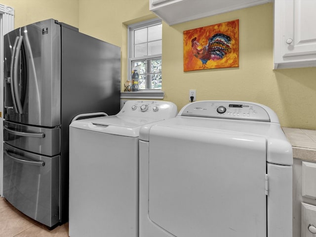 laundry area with separate washer and dryer, light tile patterned floors, and cabinets