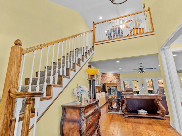 stairs with lofted ceiling, a brick fireplace, hardwood / wood-style flooring, ceiling fan, and decorative columns