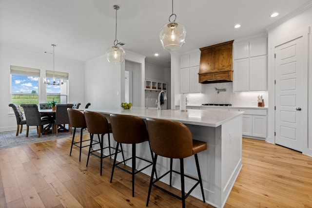 kitchen with a spacious island, a kitchen bar, custom range hood, pendant lighting, and white cabinets