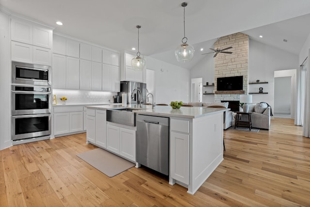 kitchen with stainless steel appliances, tasteful backsplash, white cabinets, a center island with sink, and decorative light fixtures