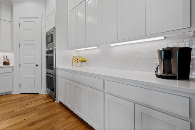 kitchen with tasteful backsplash, appliances with stainless steel finishes, white cabinets, and light wood-type flooring