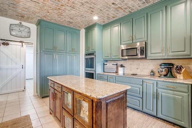 kitchen with a barn door, brick ceiling, appliances with stainless steel finishes, and light stone countertops