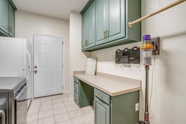 kitchen featuring light tile patterned floors, washer and clothes dryer, green cabinets, built in desk, and white fridge