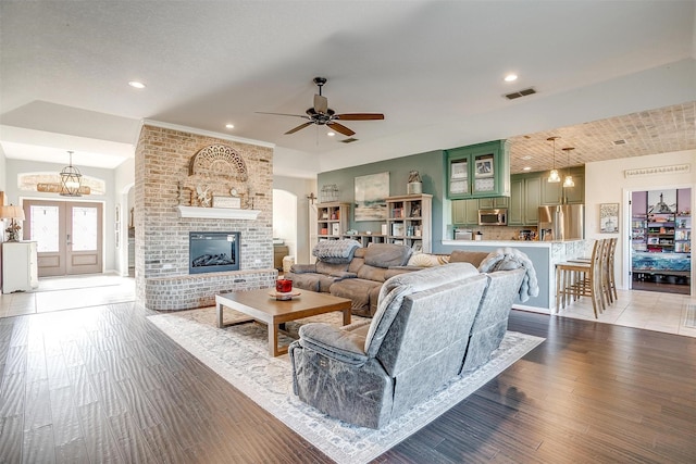 living room featuring a fireplace, french doors, ceiling fan, and light wood-type flooring