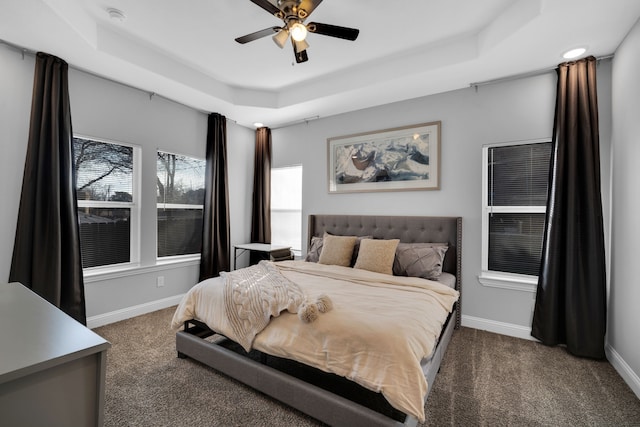 bedroom with ceiling fan, dark carpet, and a tray ceiling