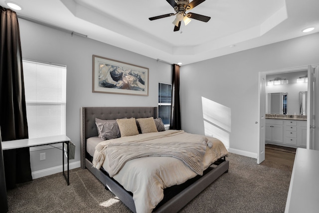 bedroom with a tray ceiling, ensuite bath, ceiling fan, and dark colored carpet