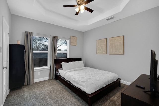 carpeted bedroom with a raised ceiling and ceiling fan