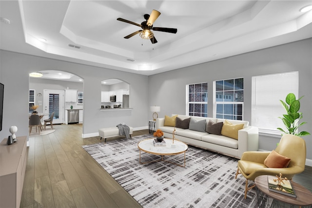 living room with hardwood / wood-style flooring, ceiling fan, and a tray ceiling