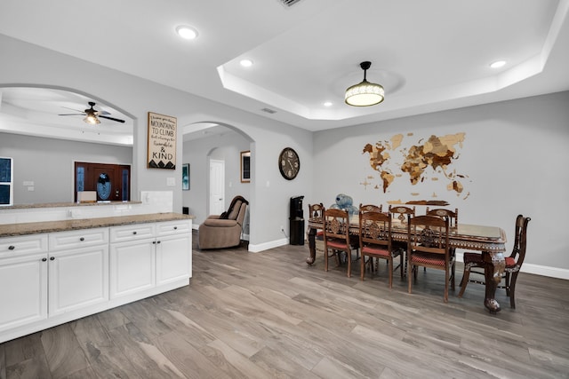 dining space with light hardwood / wood-style flooring, ceiling fan, and a tray ceiling