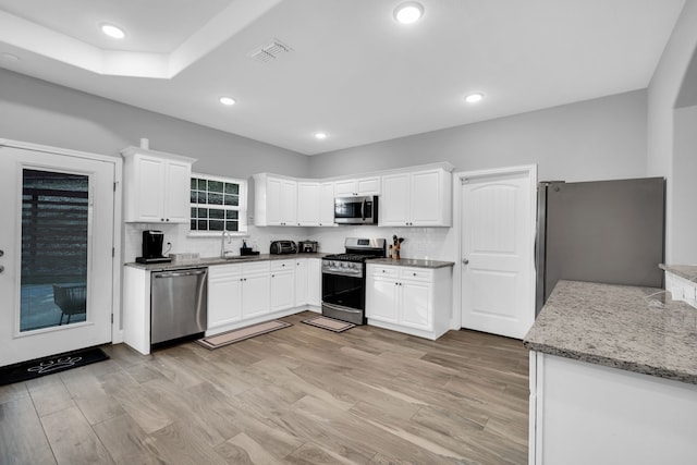 kitchen with sink, light hardwood / wood-style flooring, appliances with stainless steel finishes, white cabinetry, and light stone countertops