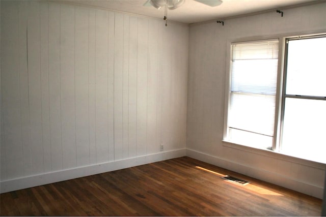 spare room with dark hardwood / wood-style floors, wooden walls, and ceiling fan