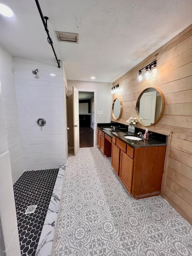 bathroom with vanity, wooden walls, a textured ceiling, and a tile shower