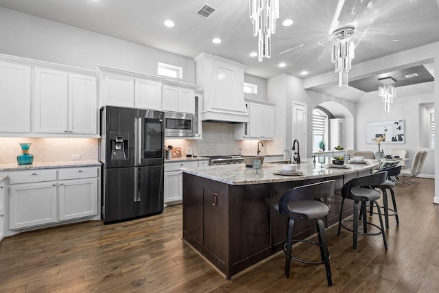 kitchen featuring arched walkways, white cabinetry, visible vents, appliances with stainless steel finishes, and custom range hood