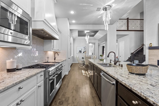 kitchen featuring visible vents, white cabinets, custom exhaust hood, stainless steel appliances, and a sink